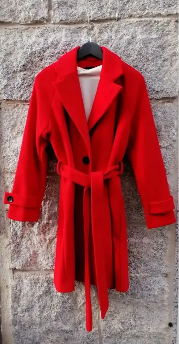Foto original: abrigo de lana rojo con cinturón colgado en una percha sobre una pared de piedra