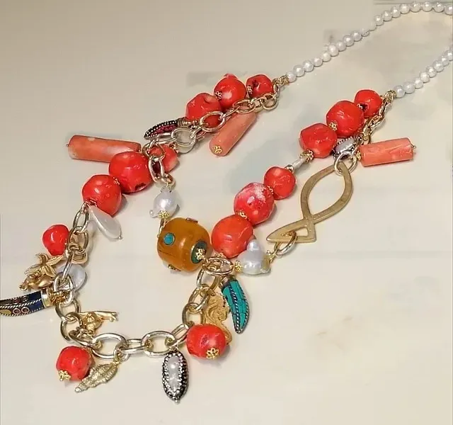 Foto original: collar artesanal de coral rojo, perlas, cadena dorada y dijes colgado sobre una superficie clara