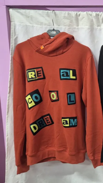 Foto original: sudadera naranja con capucha y parches de colores colgada en una percha
