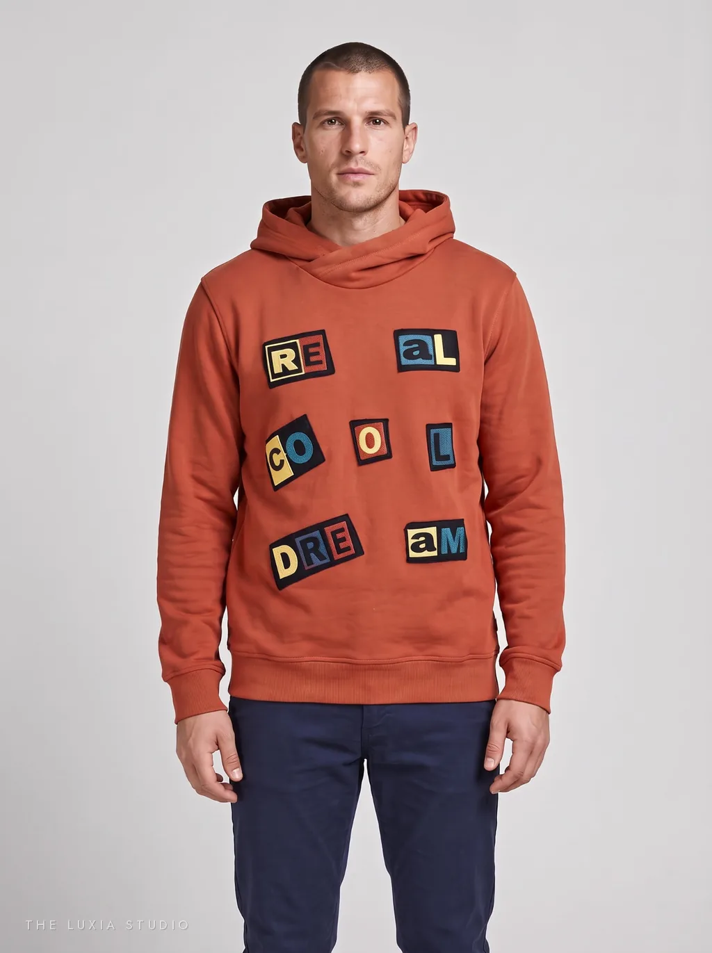 Después, estudio: modelo creada con IA con la misma sudadera naranja con parches sobre fondo neutro claro
